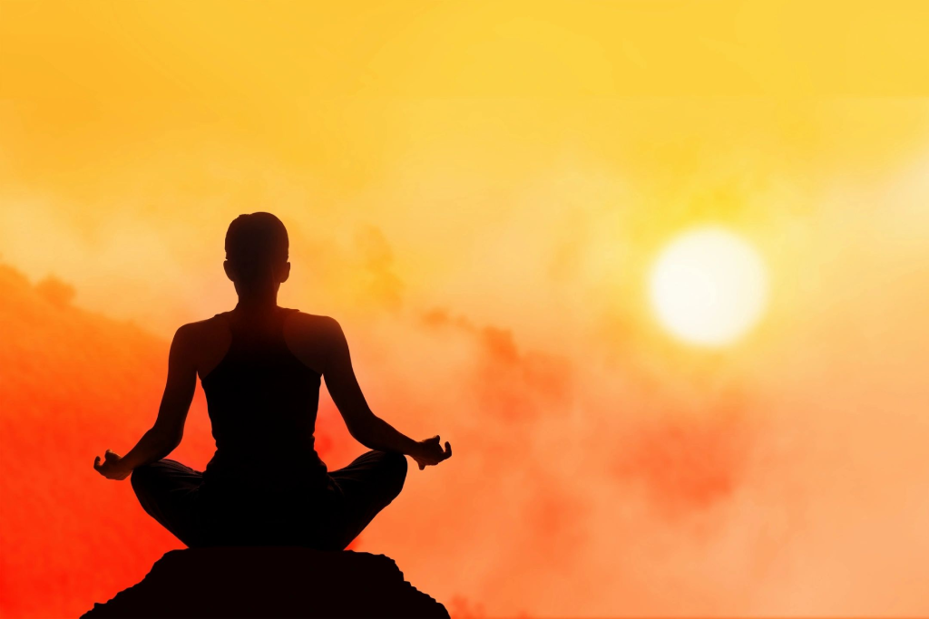 A person sitting in the sun with their hands in yoga pose.