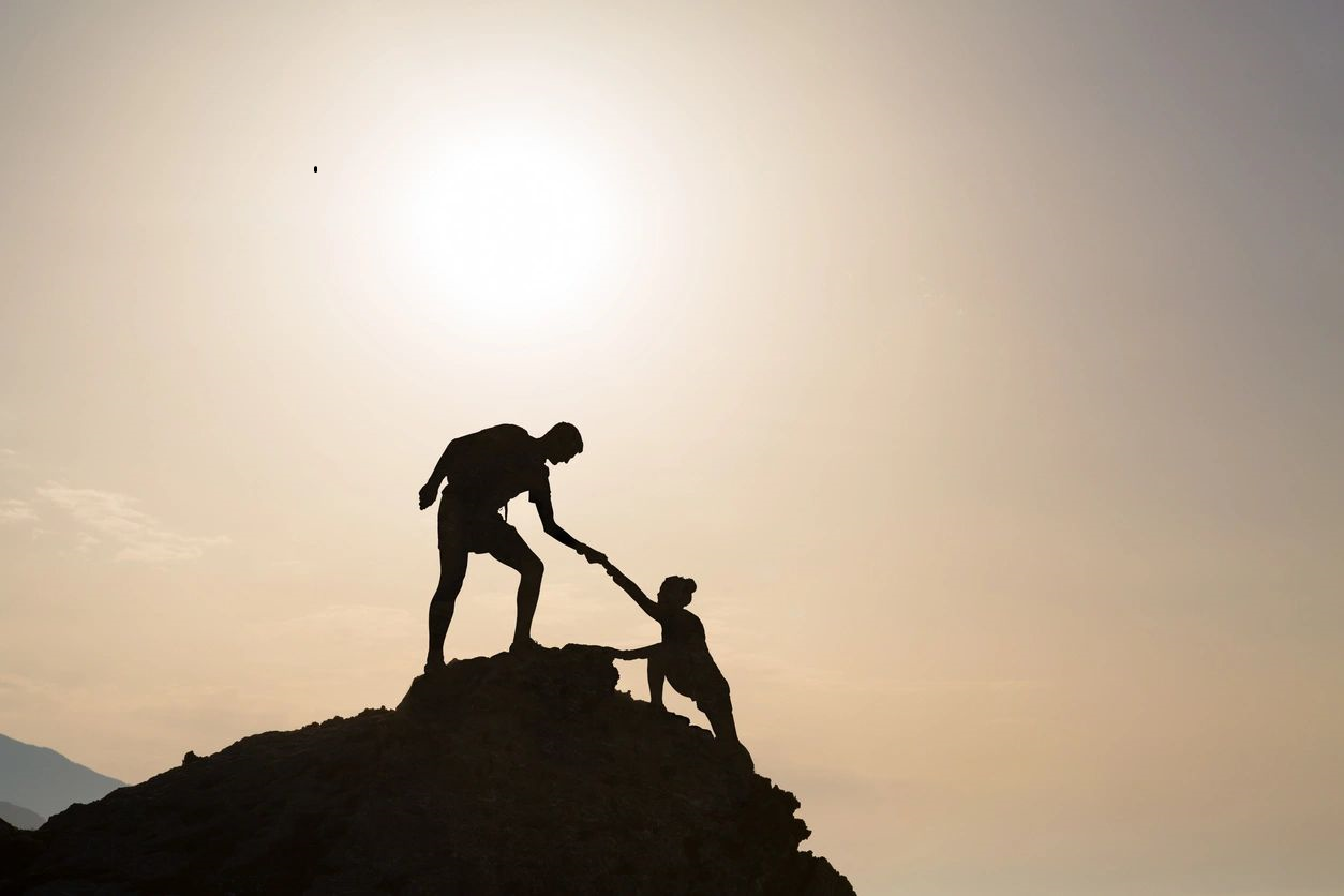 A man helping another person climb up the side of a hill.