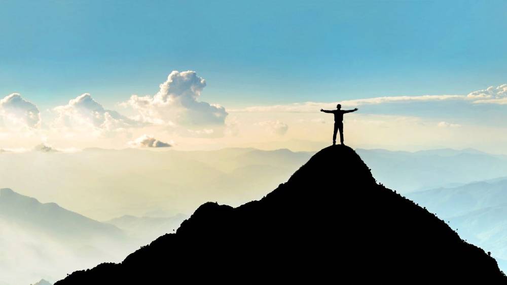 A person standing on top of a mountain with arms outstretched.