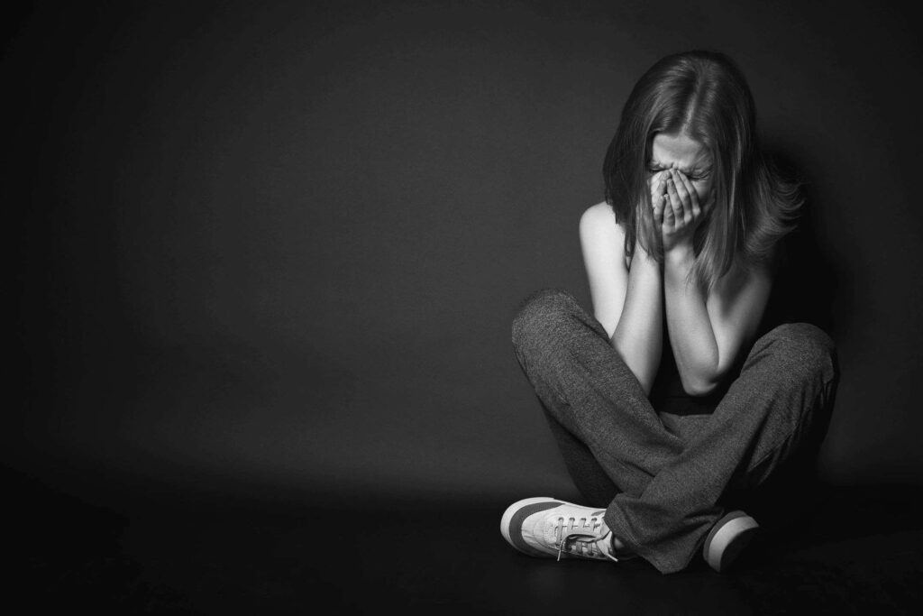 A woman sitting on the ground with her hands covering her face.