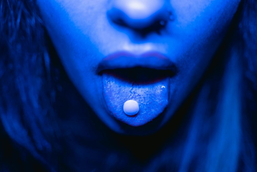 A woman with blue skin and white pill in her mouth.